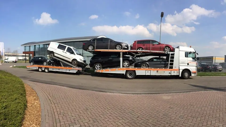 Volgeladen autotransporter met personenauto's op twee laadvloeren, langs de weg
